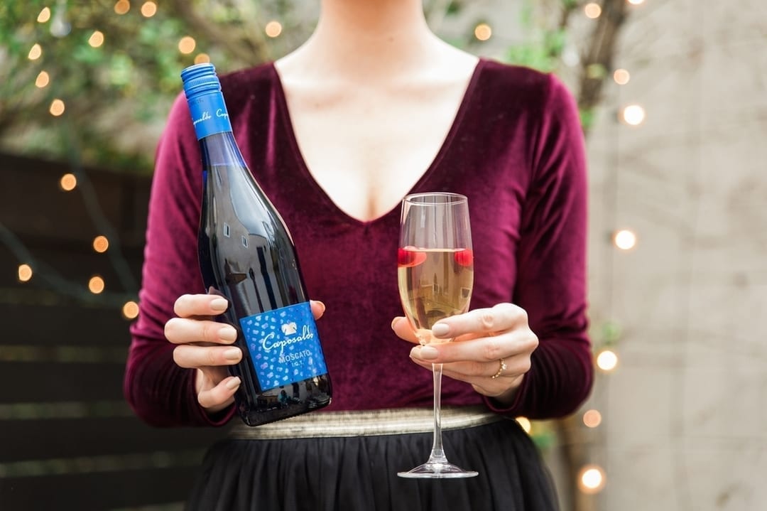 Woman holding glass of sparkling wine and bottle of Caposaldo Moscato