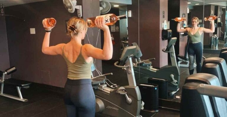 Woman lifting AIX Provence France French rose magnum wine bottles in a gym in front of mirror