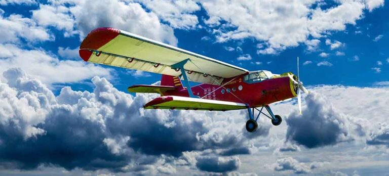 Old propeller airplane flying through a blue sky with clouds in the background