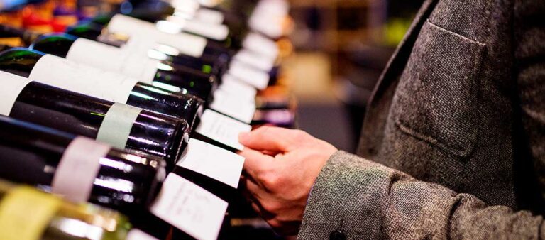 Person checking wine rating review on shelf talker in wine retail shop