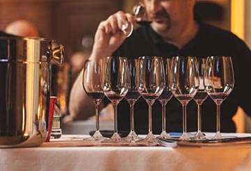 Wine critic John Fodera sniffing glass of wine behind several other glasses of red wine