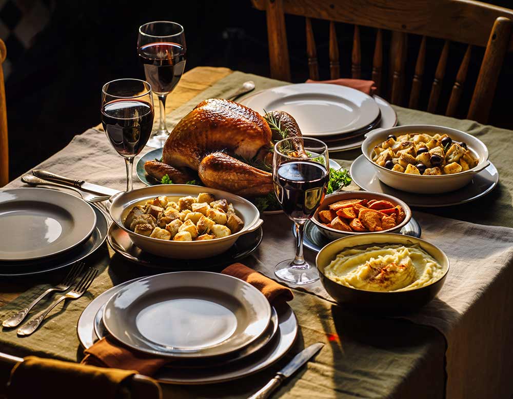 Traditional Thanksgiving dinner with roast turkey, roasted carrots, mashed potatoes, stuffing, and glasses of red wine on a table