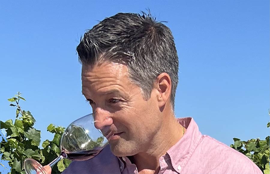 Wine Educator Nick Poletto dipping his nose into a wine glass to smell red wine with a vineyard in the background